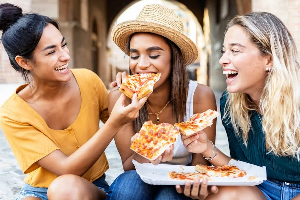 three women eating one of the popular street food, pizza, while sitting in the street - Chef's Deal