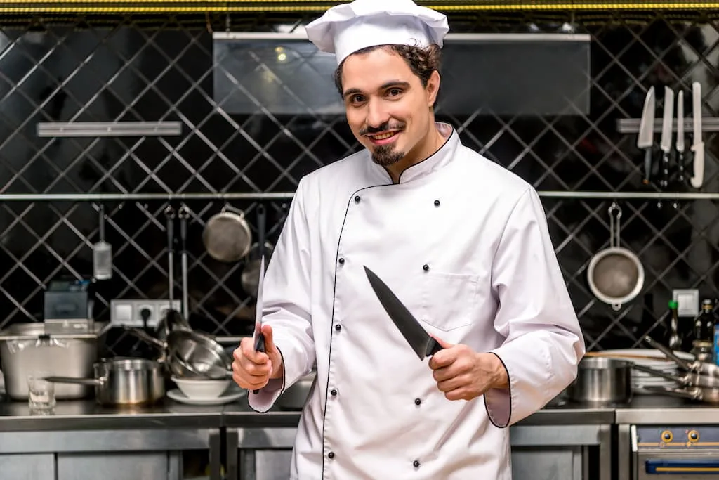 A chef with commercial kitchen knives in a kitchen and smiling - Chef's Deal
