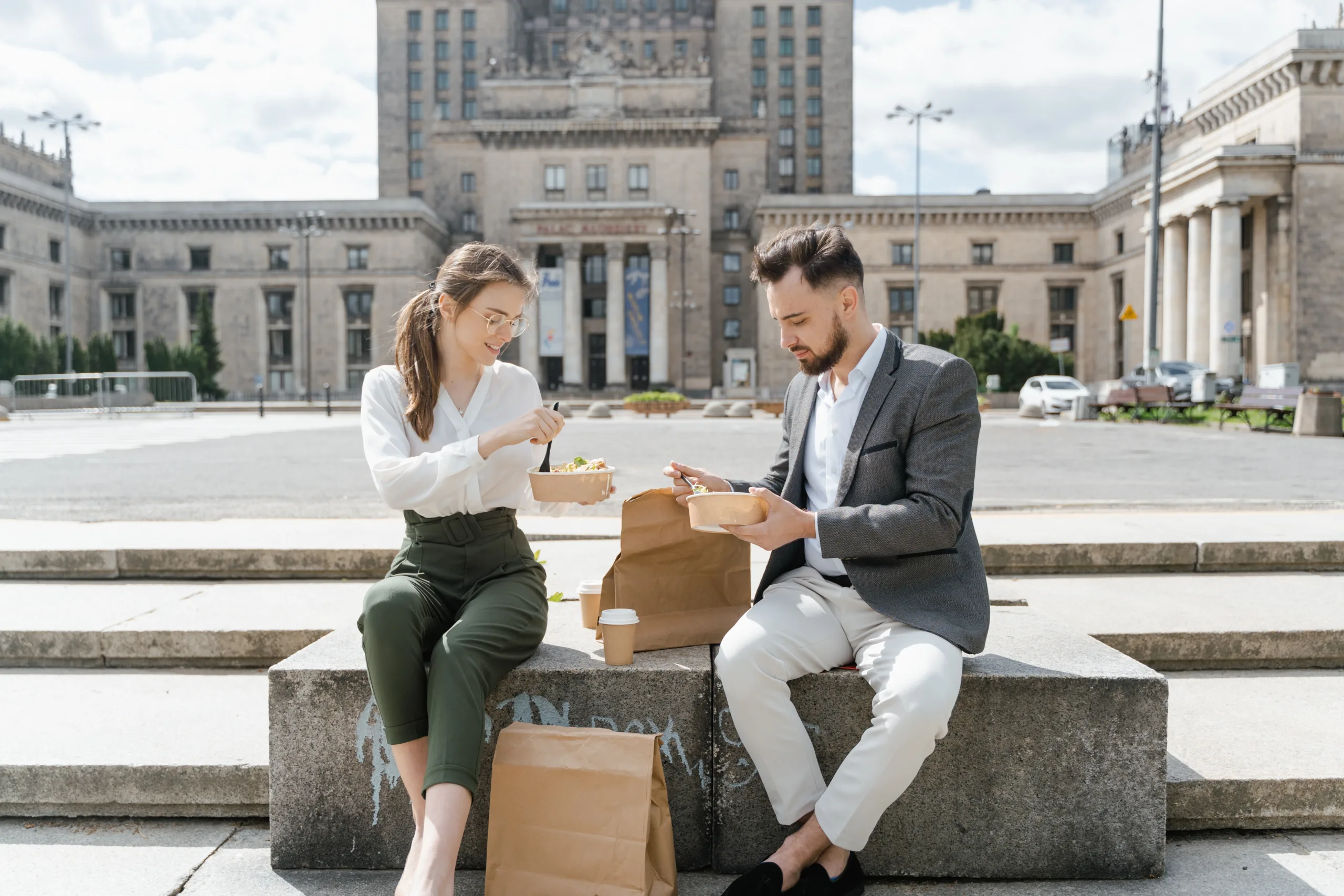 How to optimize a commercial kitchen for delivery and takeout? - Man and woman sitting on a stone bench and opening takeout bags. 